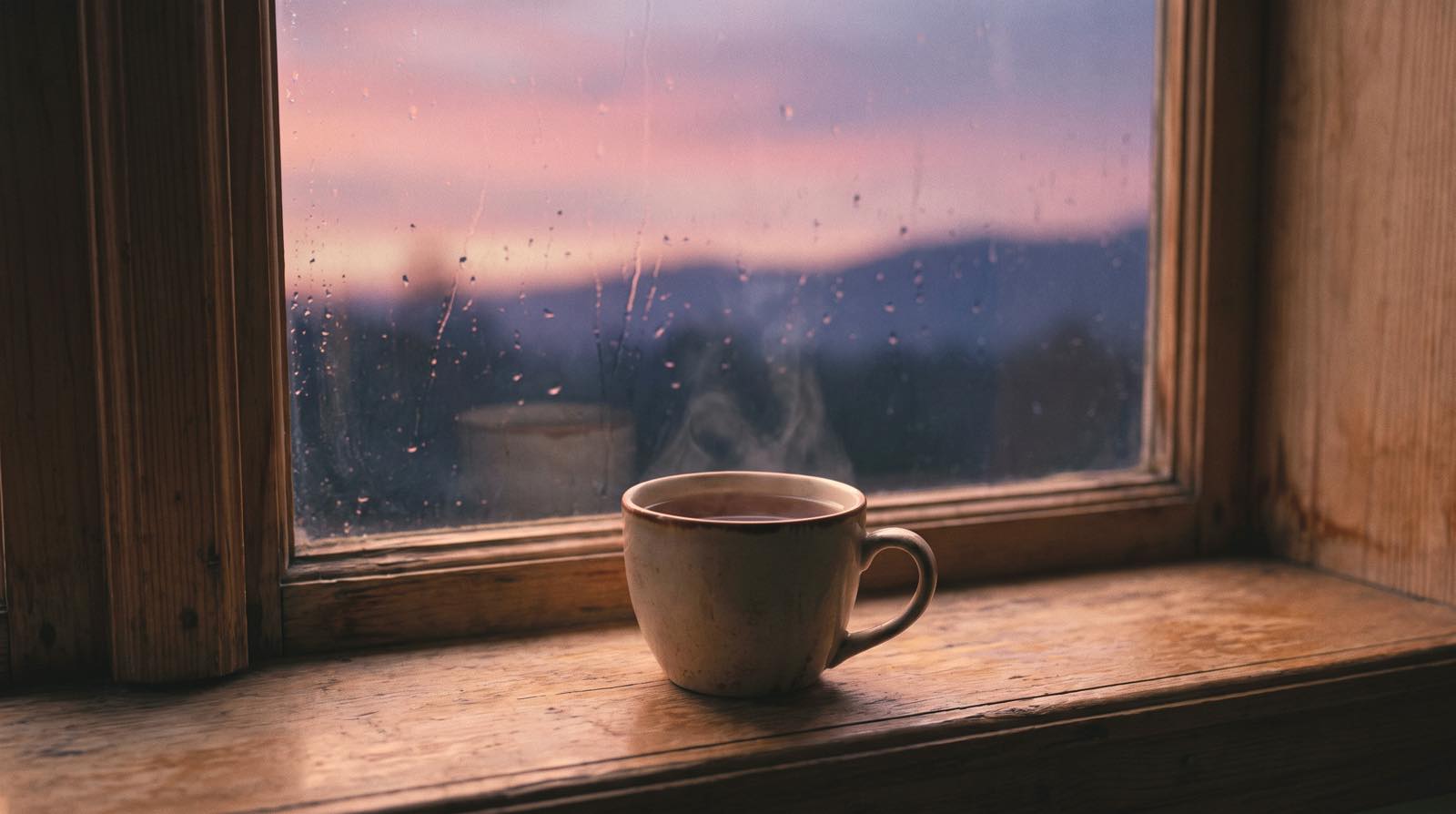 A steaming mug on a windowsill at dusk