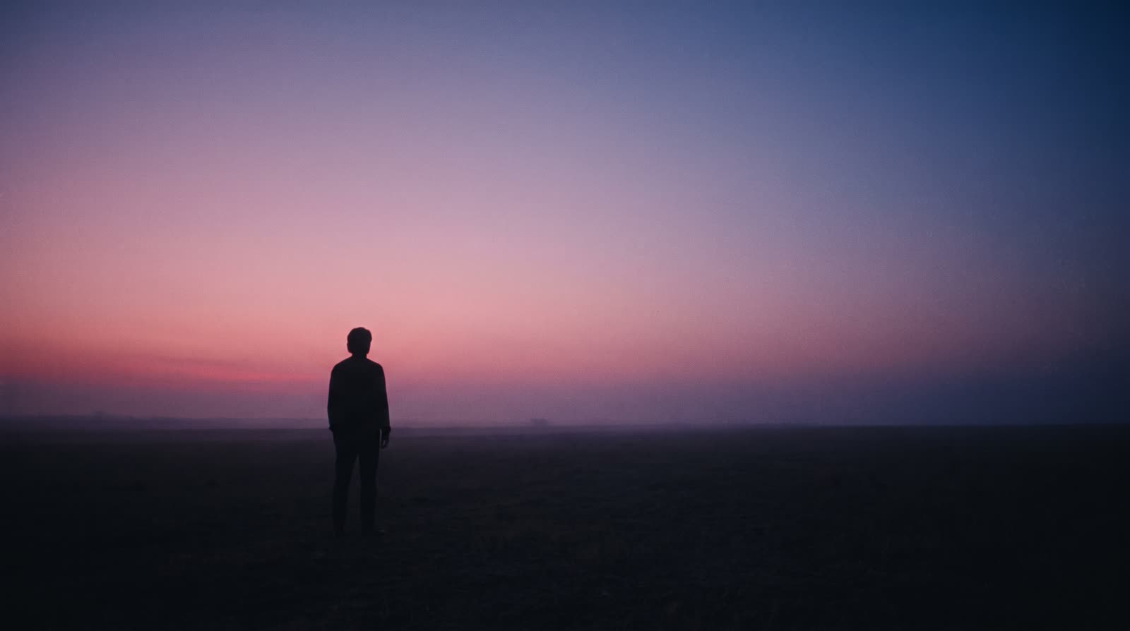 A person standing alone under a twilight sky at dusk